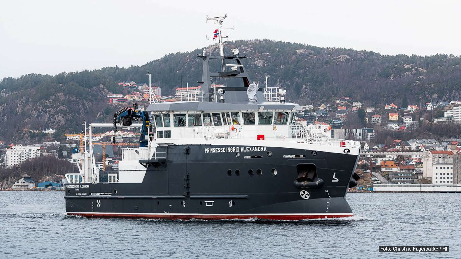 Forskningsfartøyet Prinsesse Ingrid Alexandra seiler i Byfjorden med by og fjell i bakgrunnen.