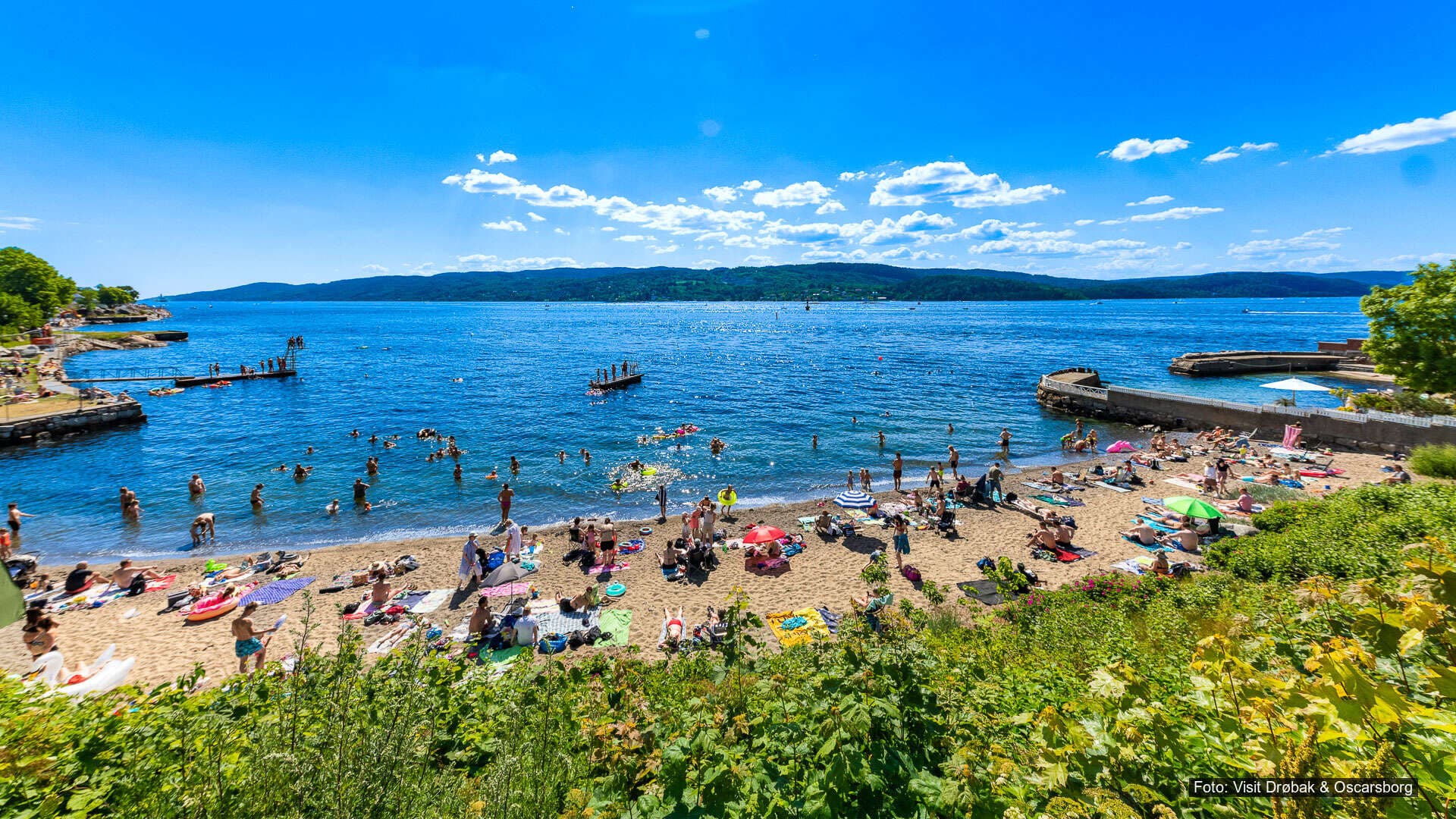 Sommerdag på Parrstranda i Drøbak Mange mennesker bader og soler seg på sandstrand ved fjorden på en solrik sommerdag.